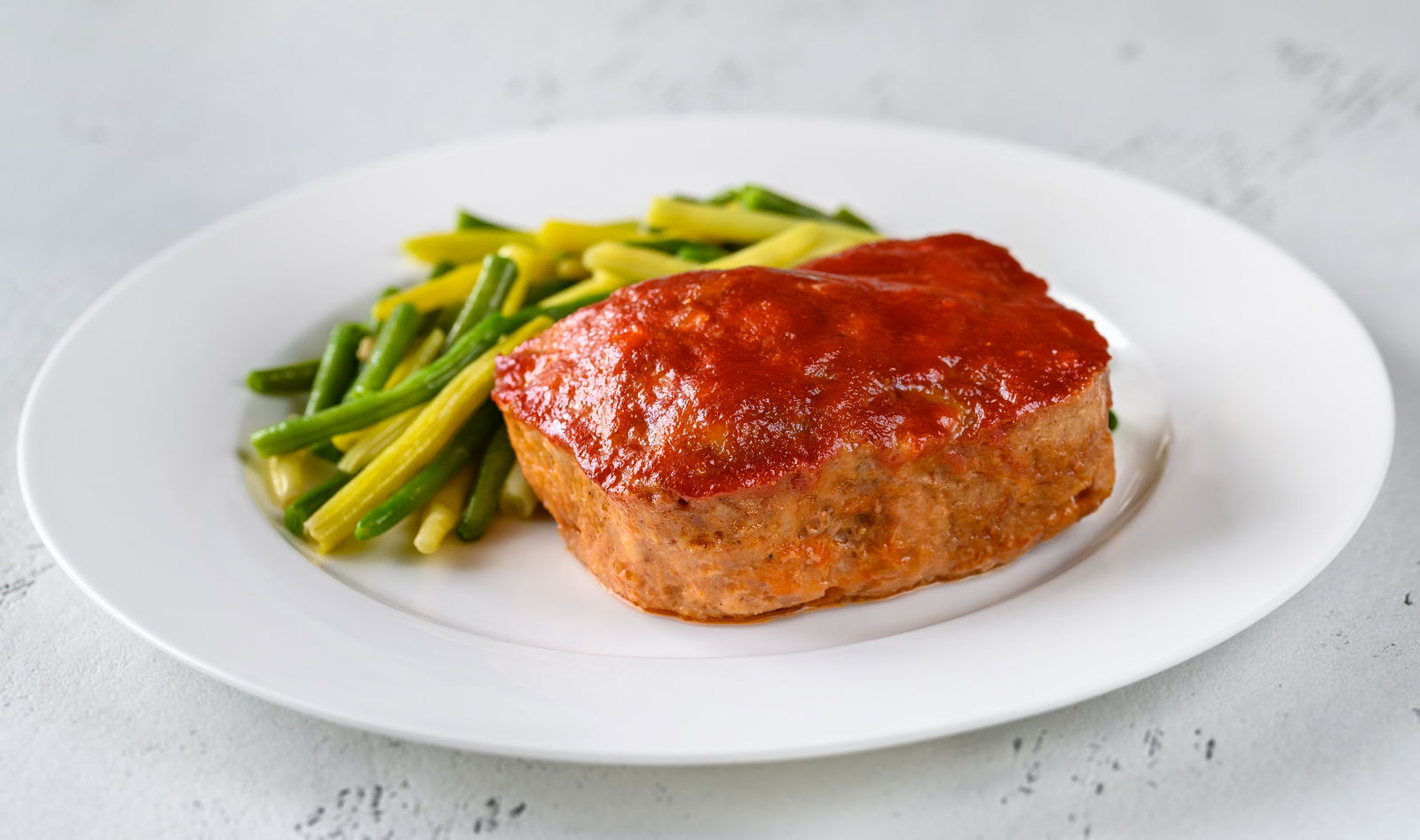 Meatloaf topped with tomato sauce with green beans.
