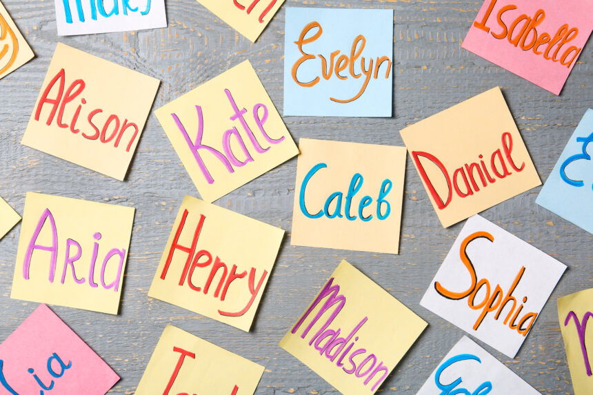 Colorful paper sheets with written different baby names on grey wooden table, flat lay