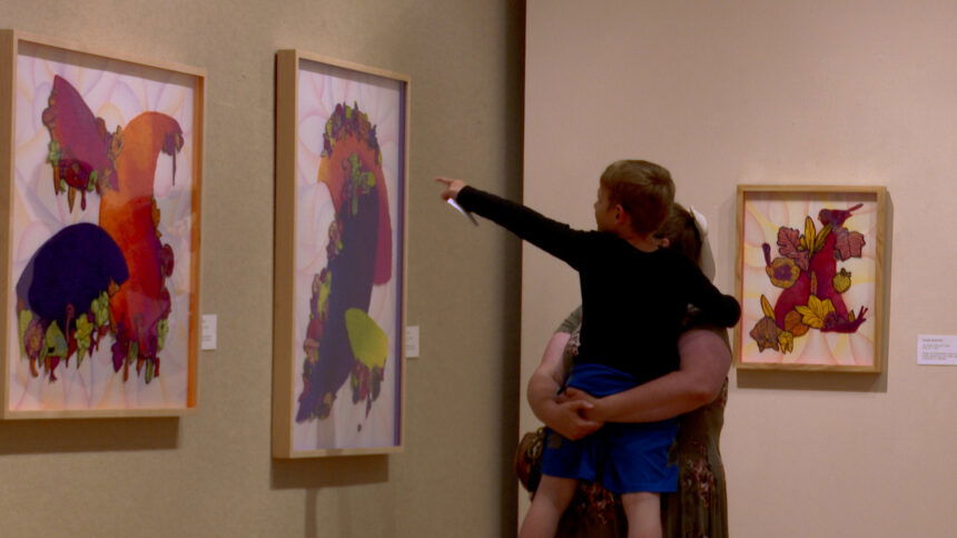 A boy in his mother's arms points at art hanging on the wall