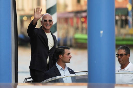 Amazon multi-billionaire founder Jeff Bezos waves as he leaves by boat a hotel in Venice