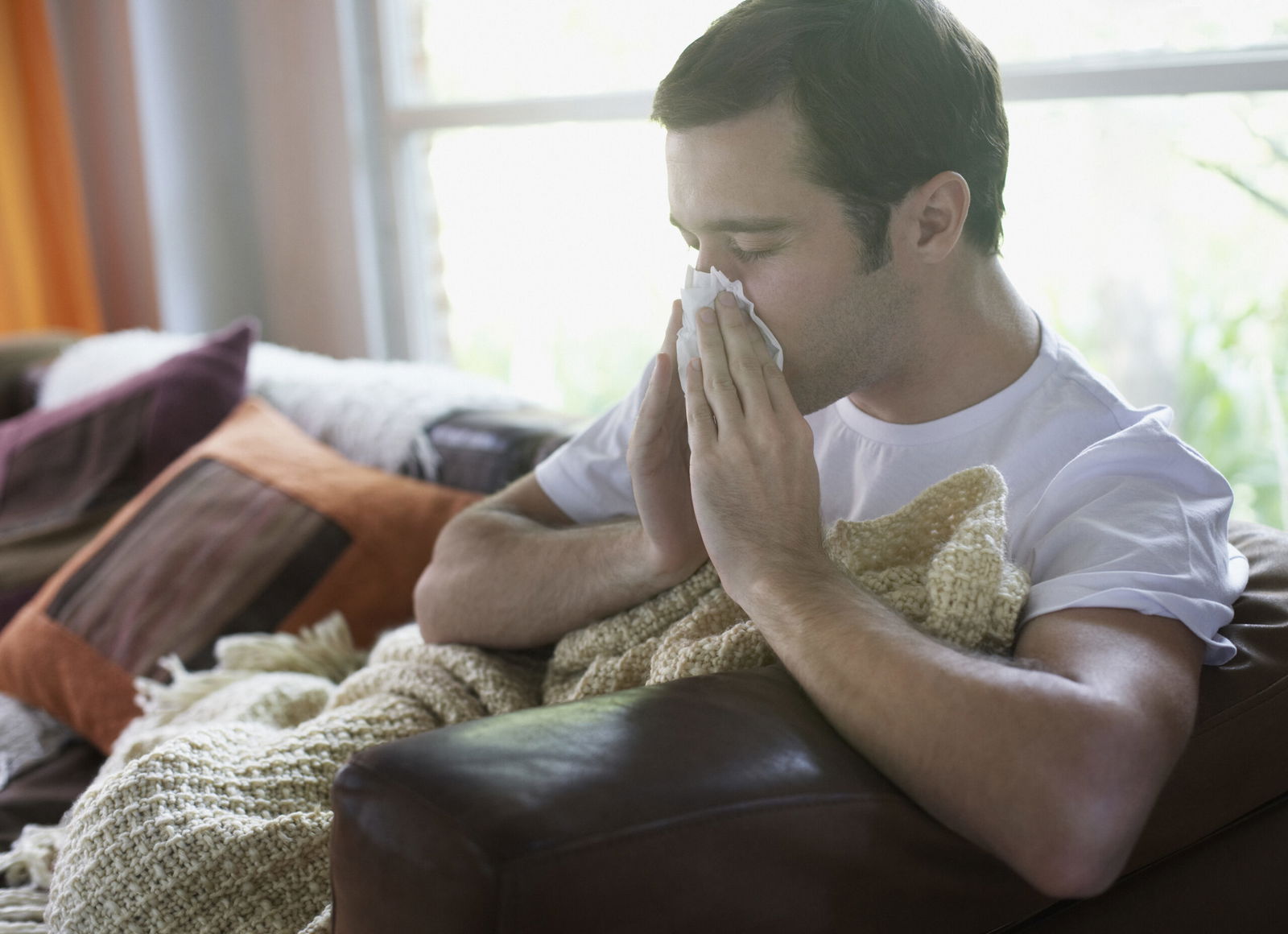 Man sitting in living room blowing nose.