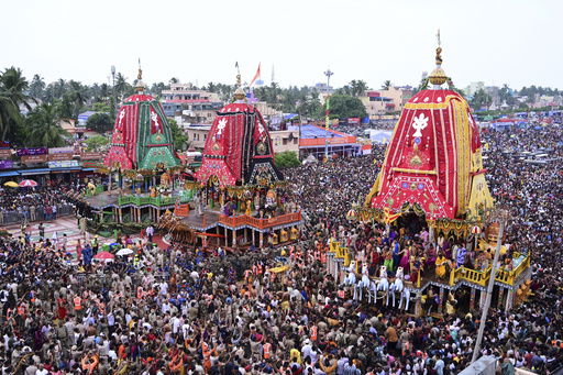 Hindu devotees walk in a procession accompanying three large chariots housing deities