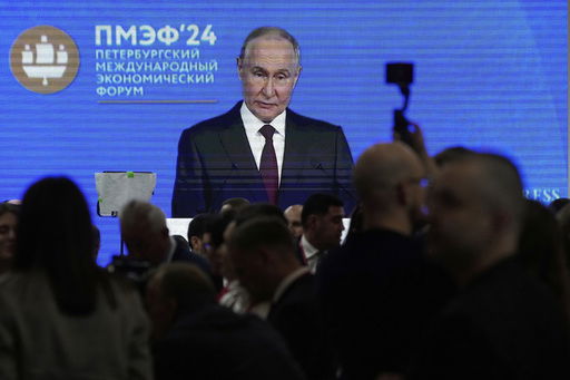 Guests and participants walk in front of a TV screen showing Russian President Vladimir Putin on the sidelines of the St. Petersburg International Economic Forum in St. Petersburg