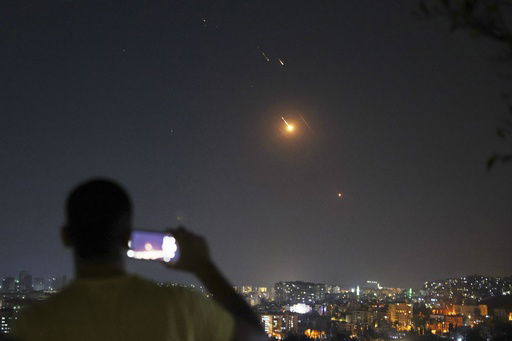 A man takes a cellphone photo as missiles fired from Iran toward Israel fly over Syrian territory in Damascus