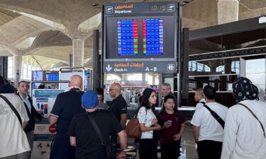 People stand in front of a flight information display screen showing information about delayed and canceled flights at Queen Alia International Airport in Amman