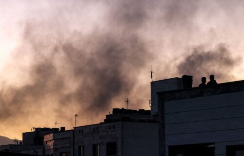 People stand on a rooftop amid billowing smoke following an overnight Israeli strike in Tehran