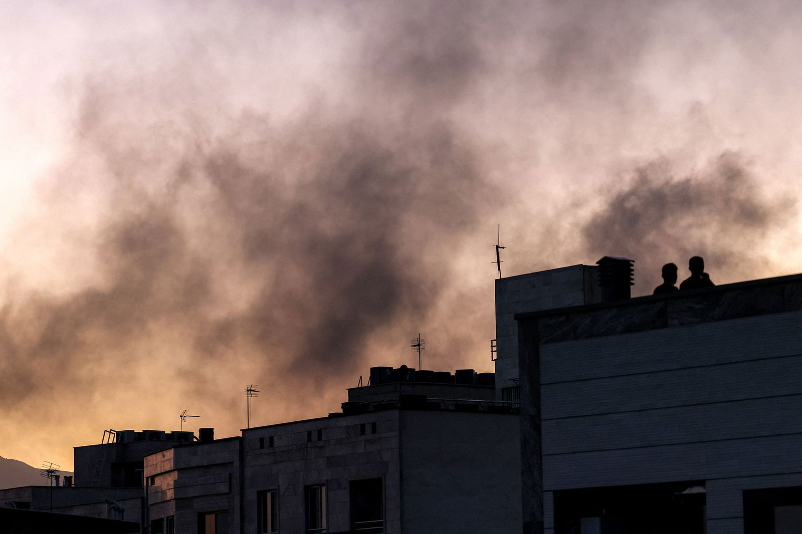 <i>Atta Kenare/AFP/Getty Images via CNN Newsource</i><br/>People stand on a rooftop amid billowing smoke following an overnight Israeli strike in Tehran