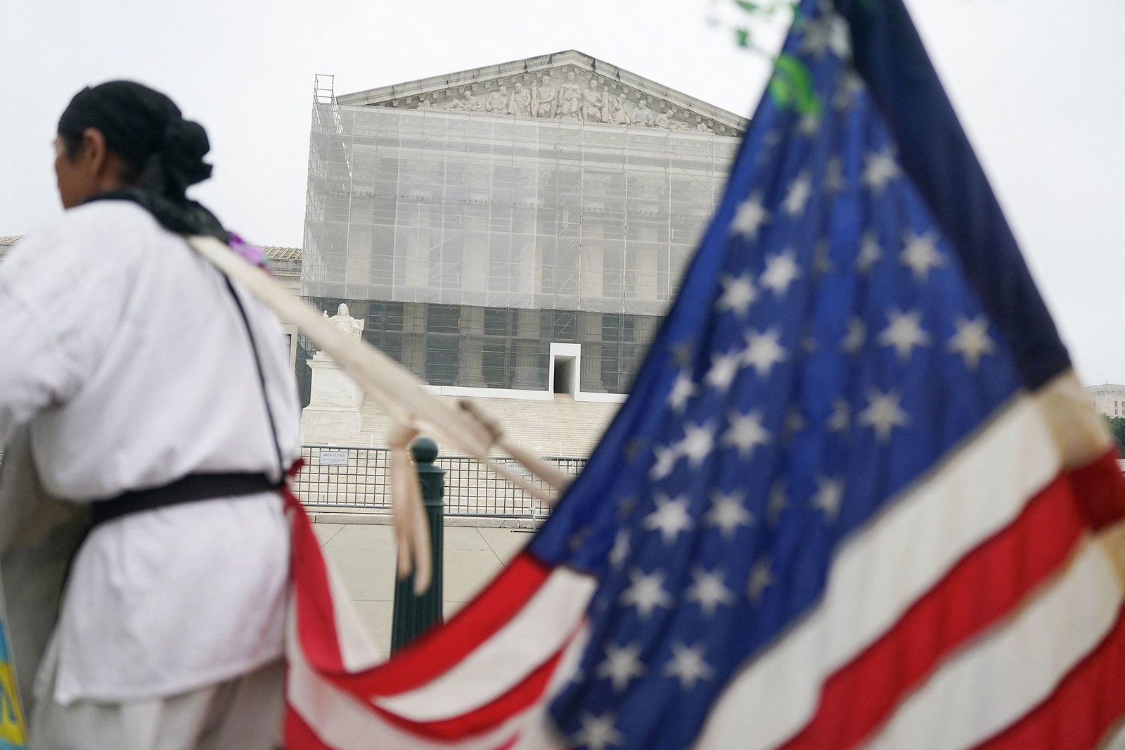 <i>Nathan Howard/Reuters via CNN Newsource</i><br/>A person stands with a US flag attached to them