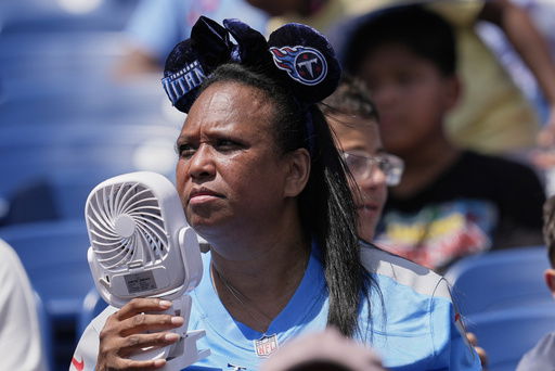 A Tennessee Titans fan uses a fan to keep cool while watching practice during