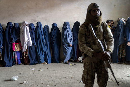 FILE - A Taliban fighter stands guard as women wait to receive food rations distributed by a humanitarian aid group in Kabul