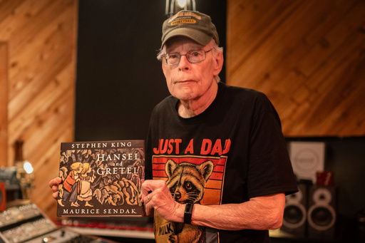 This image released by HarperCollins shows author Stephen King holding up a copy of his retelling of the Grimm fairy tale “Hansel and Gretel