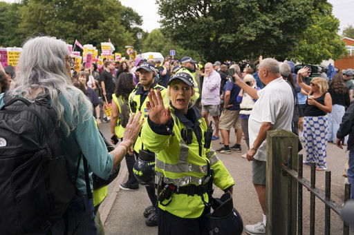A police officer reacts as demonstrators hold placards and banners as they leave a protest outside the Bell Hotel in Epping