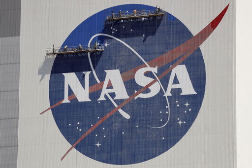 FILE - Workers on scaffolding repaint the NASA logo near the top of the Vehicle Assembly Building at the Kennedy Space Center in Cape Canaveral