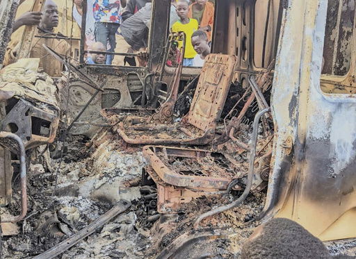 People gather around the charred remains of a burned vehicle following a deadly attack in Komanda
