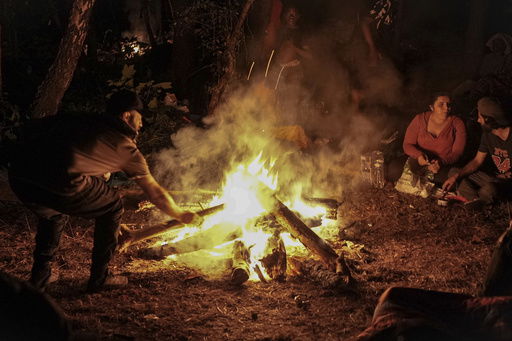 Migrants gather by a campfire in the Ecault forest