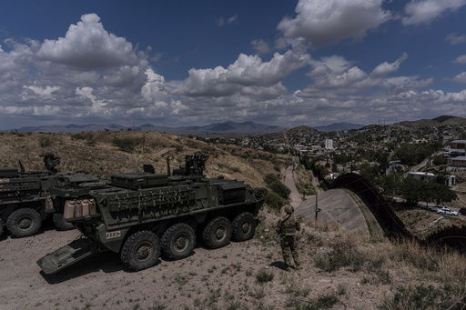 U.S. Army Sgt. Salvador Hernandez stands beside Stryker combat vehicles while watching over the U.S.-Mexico border fence from a hilltop in Nogales