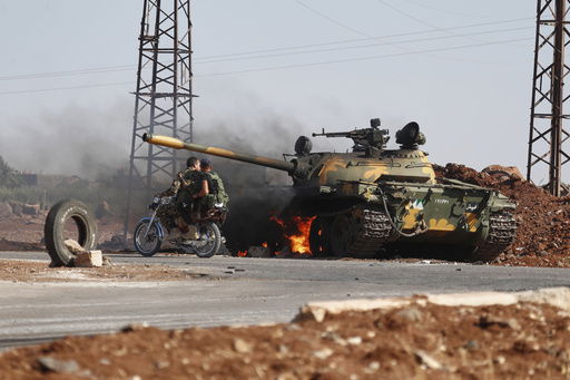 Syrian government soldiers on a motorcycle pass by a burning tank on the outskirts of Sweida city
