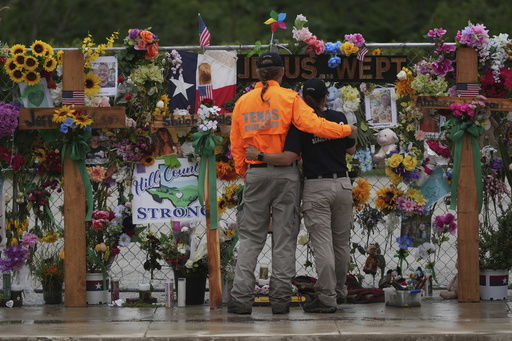 FILE - Members of a search and rescue team embrace as they visit a memorial wall for flood victims