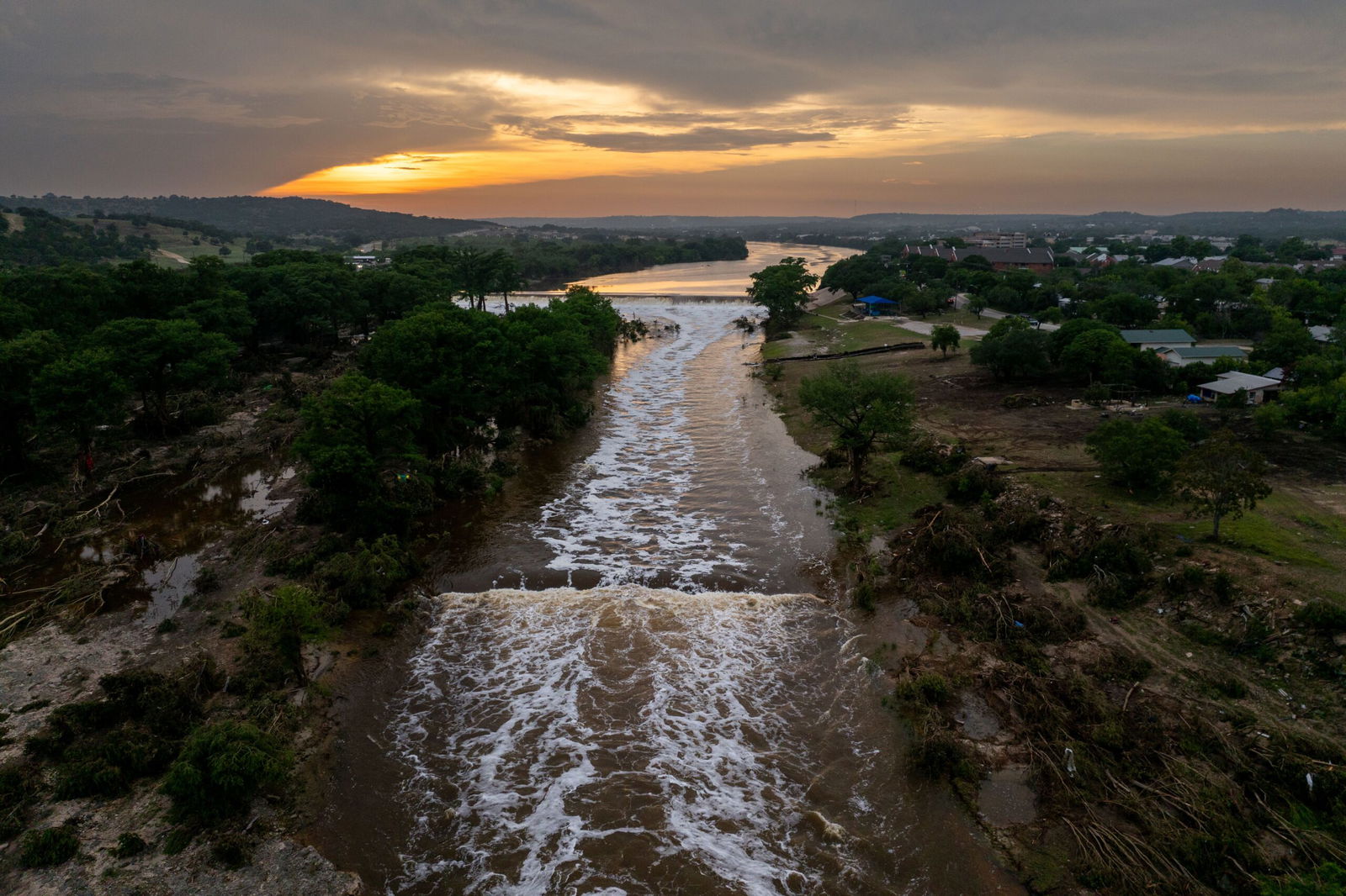 <i>Ronaldo Schemidt/AFP via Getty Images via CNN Newsource</i><br/>A search and rescue team floats Monday along the Guadalupe River past a damaged building at Camp Mystic in Hunt