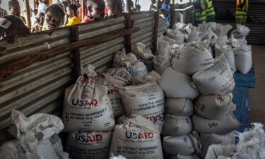 Congolese refugees look through a corrugated metal fence at the final batches of food delivered by the now-dismantled United States Agency for International Development (USAID) in a storage and food delivery area at the Musenyi refugee site in Giharo