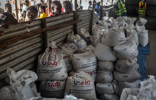 Congolese refugees look through a corrugated metal fence at the final batches of food delivered by the now-dismantled United States Agency for International Development (USAID) in a storage and food delivery area at the Musenyi refugee site in Giharo