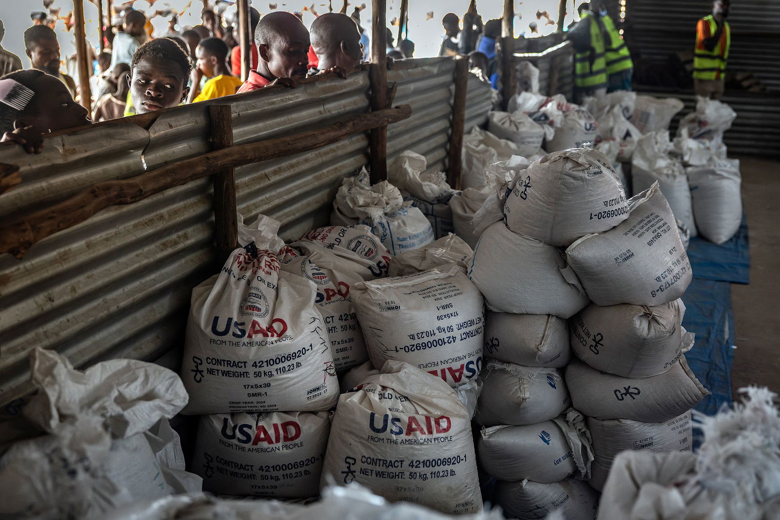 <i>Luis Tato/AFP/Getty Images via CNN Newsource</i><br/>Congolese refugees look through a corrugated metal fence at the final batches of food delivered by the now-dismantled United States Agency for International Development (USAID) in a storage and food delivery area at the Musenyi refugee site in Giharo