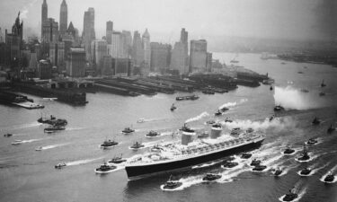 A huge cordon of tugs accompanies the SS United States past the New York skyline on June 23
