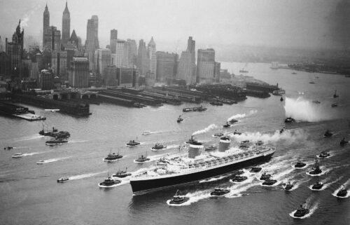 A huge cordon of tugs accompanies the SS United States past the New York skyline on June 23