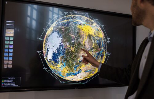A worker points to a monitor displaying current satellites in orbit and real-time communications across the globe at the Iridium Communications Inc. Satellite Network Operations Center in Leesburg